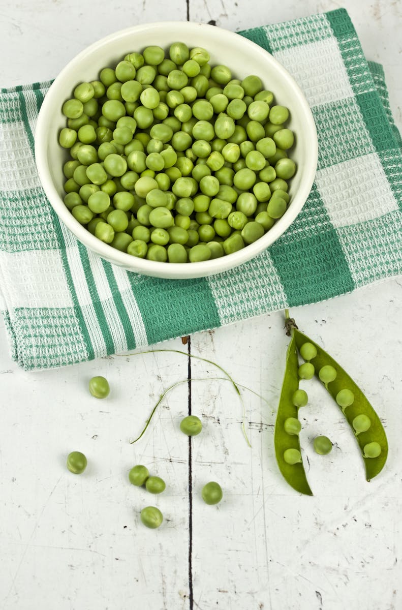 A vibrant display of green peas in a bowl with a rustic white background, ideal for food and health concepts.